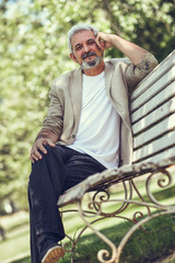 Obraz premium Pensive mature man sitting on bench in an urban park.