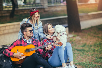 Obraz na płótnie Canvas Friends in the park having fun playing guitar