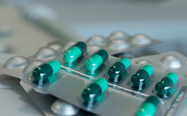 Green capsules in blister pack close up with blurry hospital background