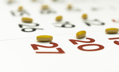 Yellow pills on a calendar isolated on white close up- medication plan or timing compliance concept