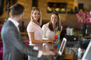 Two beautiful young women are drinking cocktails and flirting with boys at the bar