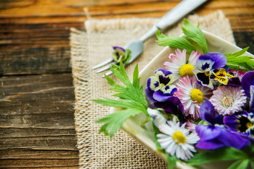 Fototapeta na wymiar Fresh salad with smoked salmon, black olives, cherry tomatoes and edible flowers on wooden background.