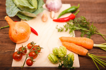 Fresh vegetables on a cutting board, on a wooden background. Chili, carrots, cherry tomatoes, hops, cabbage and greens on a wooden table. Space for text. Thanksgiving Day. View from above. Background.