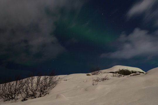 Aurora and clouds in the night sky in winter over the tundra and hills.