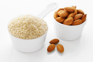 Almond flour in measuring cup with almonds on white background