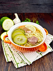 Soup with zucchini and noodles in red bowl on towel