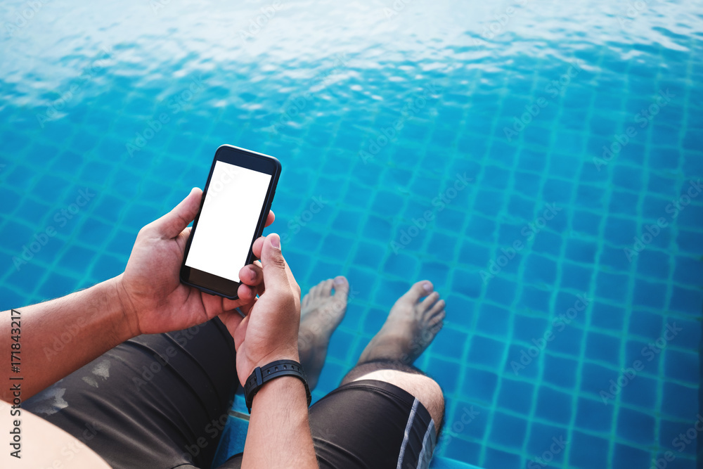 Poster a man using mobile smart phone, blank space on screen, with legs dipping in pool in summer. clipping