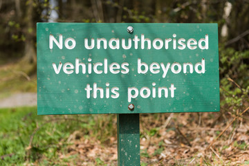 A no unauthorised vehicles beyond this point, hand carved wooden warning parking sign, on a stake with a countryside background.