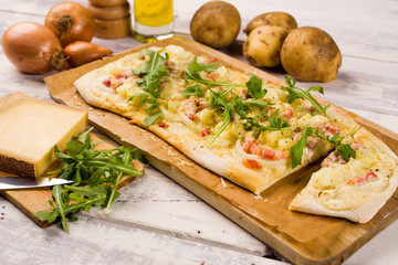 Alsatian tarte flambe or flammenkuchen or white pizza with bacon, sour cream, onions, potato and cheese on a white wooden background