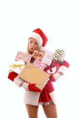 A young girl dressed in a Santa Claus suit has lots of Christmas presents gathered in her arms. Smiling, she stands in front of a white background.