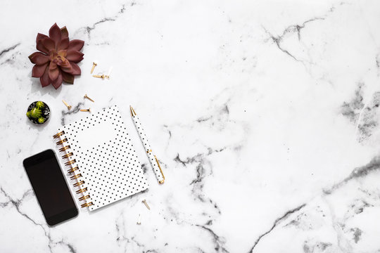 Marble table flat lay with gold stationary accessories, mobile phone, notebook and pen for office planner