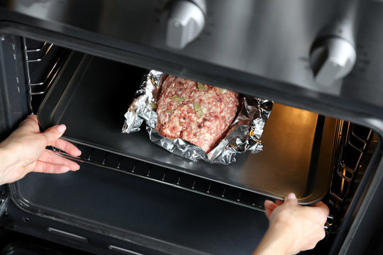 Woman putting baking tray with raw turkey meatloaf into oven