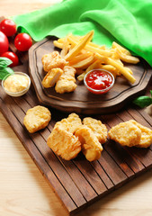 Tasty nuggets, french fries and small bowls with sauces for chicken on wooden boards