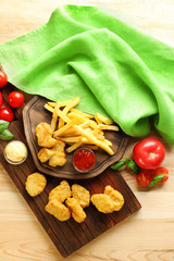 Tasty nuggets, french fries and small bowls with sauces for chicken on wooden boards