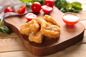 Tasty nuggets and small bowl with sauce for chicken on wooden board