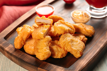 Tasty nuggets and small bowls with sauces for chicken on wooden tray