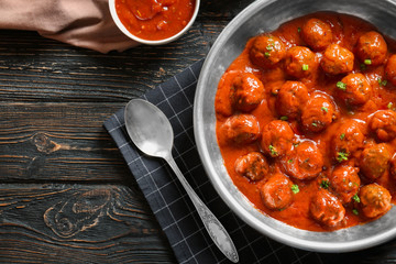 Saucepan with delicious meatballs in tomato sauce on table