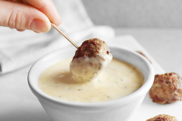 Female hand dipping delicious meatball into bowl with sauce, closeup
