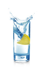 Falling lemon slice into glass with water on white background