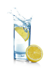 Fototapeta na wymiar Falling lemon slice into glass with water on white background