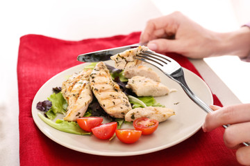 Woman eating tasty chicken meat with tomatoes on table. Cooking for one concept