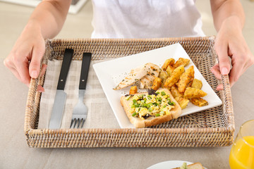 Woman holding wicker tray with dinner at table. Cooking for one concept