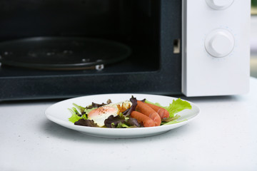 Plate with lunch near microwave oven on table. Cooking for one concept