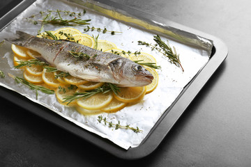 Fresh fish with slices of lemon on baking tray