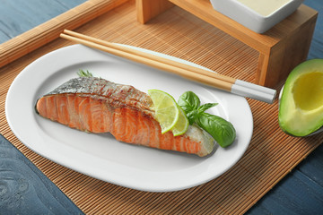 Plate with slice of delicious salmon and chopsticks on table
