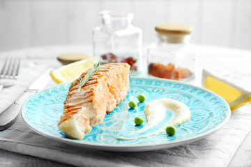 Plate with slice of salmon and delicious sauce on table