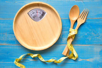 Scale shaped on the wood plate with a fork and spoon, blue background.  Diet and Healthy Concept