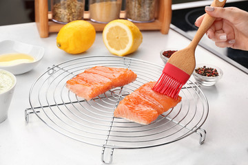 Woman applying oil on red fish fillet with silicone brush in kitchen