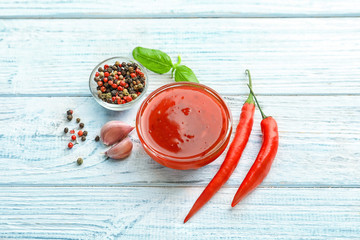 Composition with chili sauce in bowl on wooden table
