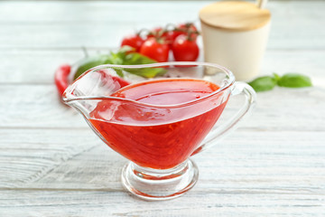 Composition with chili sauce in gravy boat on wooden table