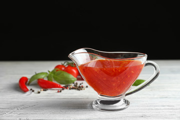 Composition with chili sauce in gravy boat on wooden table