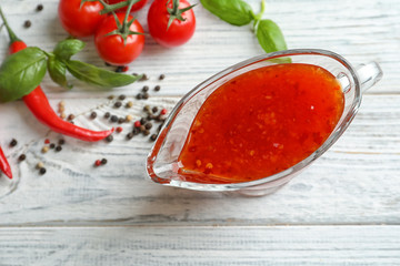 Composition with chili sauce in gravy boat on wooden table