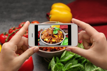 Woman taking photo of yummy stew at kitchen table