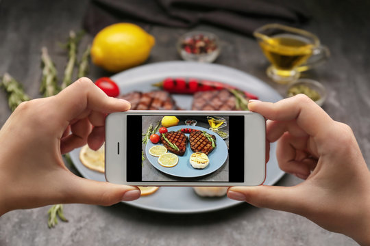 Woman taking photo of yummy grilled steaks at kitchen table