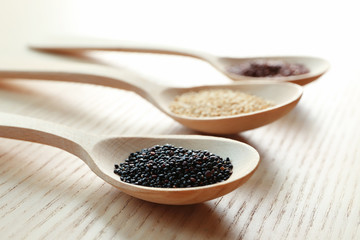 Spoons with different types of quinoa on wooden table, closeup