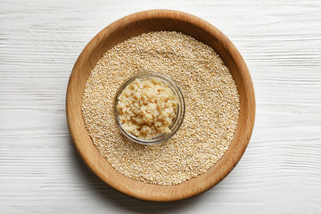 Bowls with boiled and raw quinoa grains on wooden table