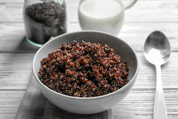 Bowl with boiled quinoa grains on wooden table