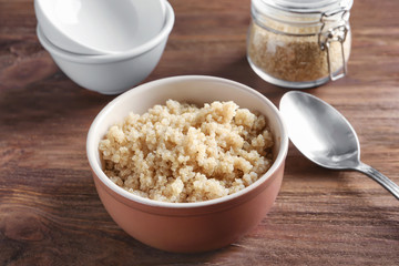 Bowl with boiled white quinoa grains on wooden table