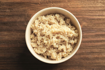 Bowl with boiled white quinoa grains on wooden table