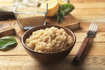 Poster Im Rahmen Bowl with boiled white quinoa grains on wooden table © Africa Studio
