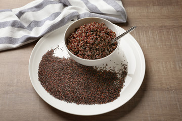Dishware with boiled and raw quinoa grains on wooden table