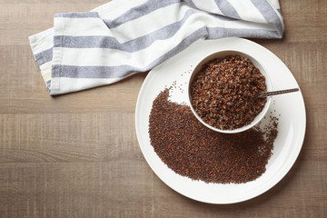 Dishware with boiled and raw quinoa grains on wooden table