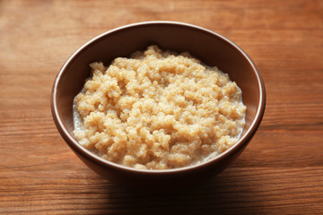 Bowl with boiled white quinoa grains on wooden table
