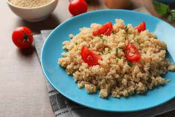 Plate with boiled quinoa grains on wooden table