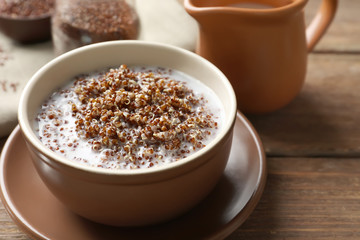 Bowl with boiled quinoa grains and milk on wooden table