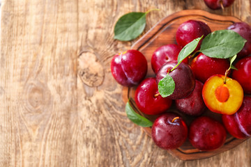 Board with fresh ripe plums on wooden table
